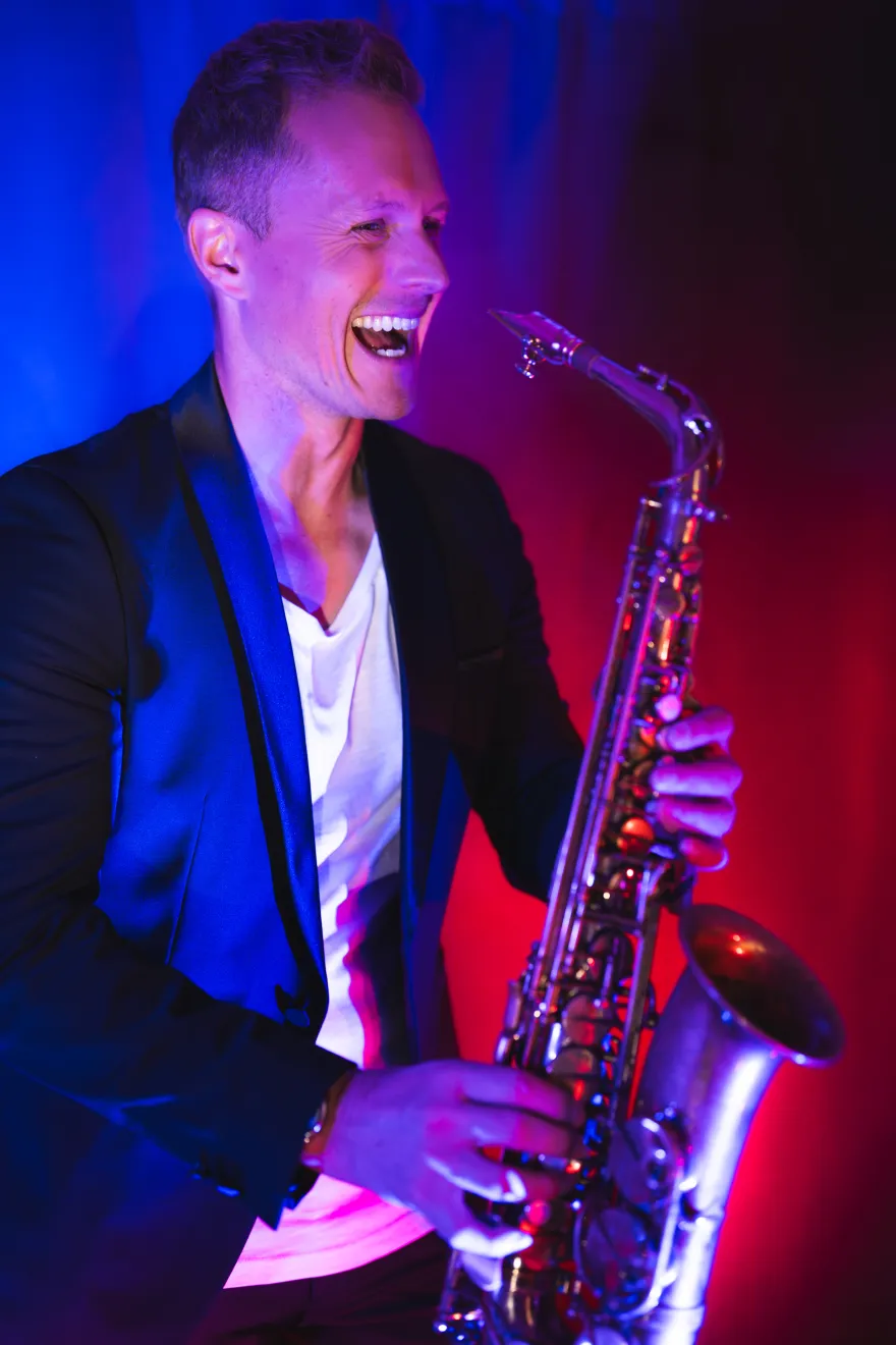 Saxophonist Philipp Schoof lacht, das Saxophon in der Hand, in blau-pinkem Bühnenlicht